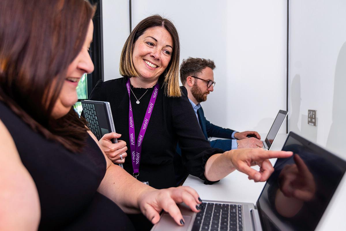A woman pointing at a laptop screen and smiling in the learning zone of the Mitie Cleaning and Hygiene Centre of Excellence